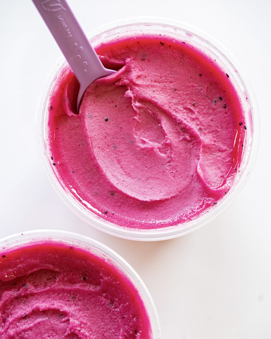 Fresh pitaya sorbet in tubs with a scooping spoon