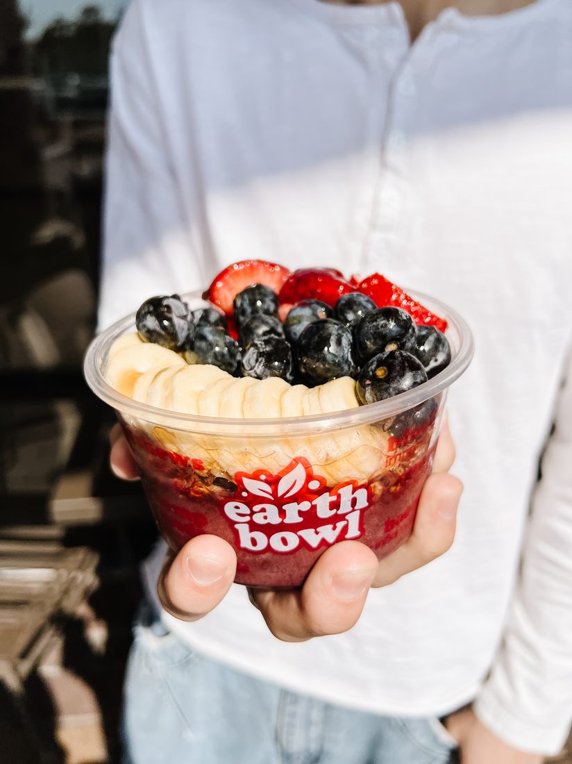 A small a&ccedil;a&iacute; bowl with banana and blueberries held outdoors